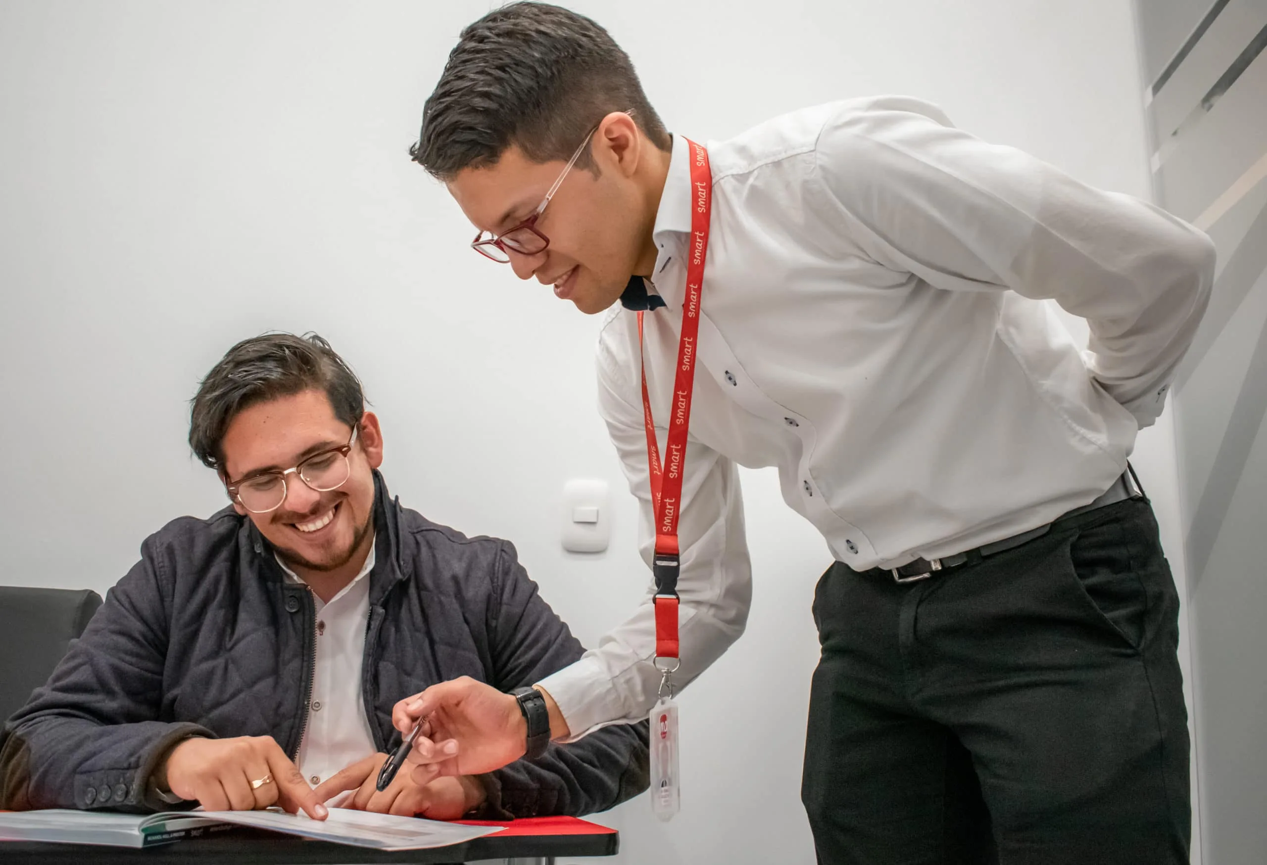 Asesor de Smart con lanyard rojo explicando un documento a un estudiante que lo firma